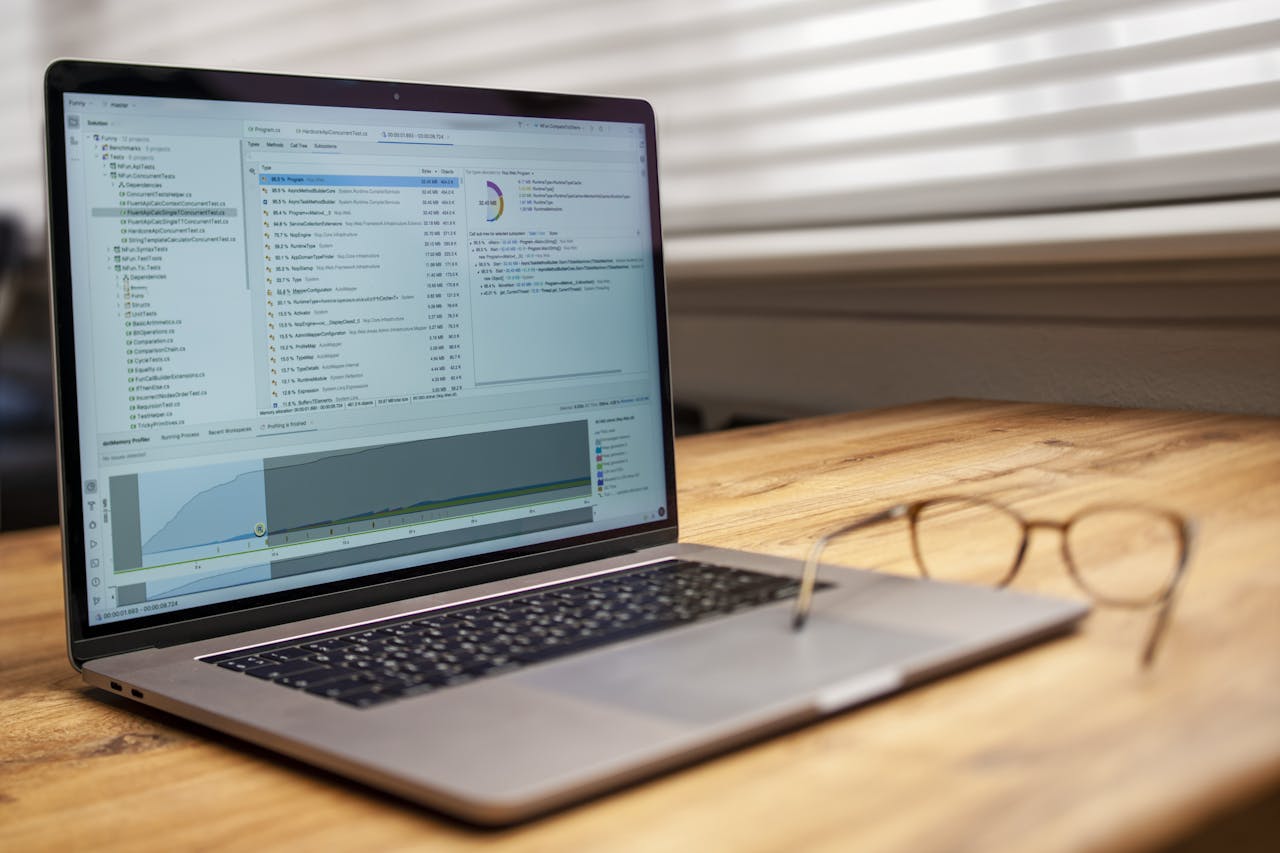 Modern laptop on a wooden desk displaying analytical software with eyeglasses nearby, indoor shot.